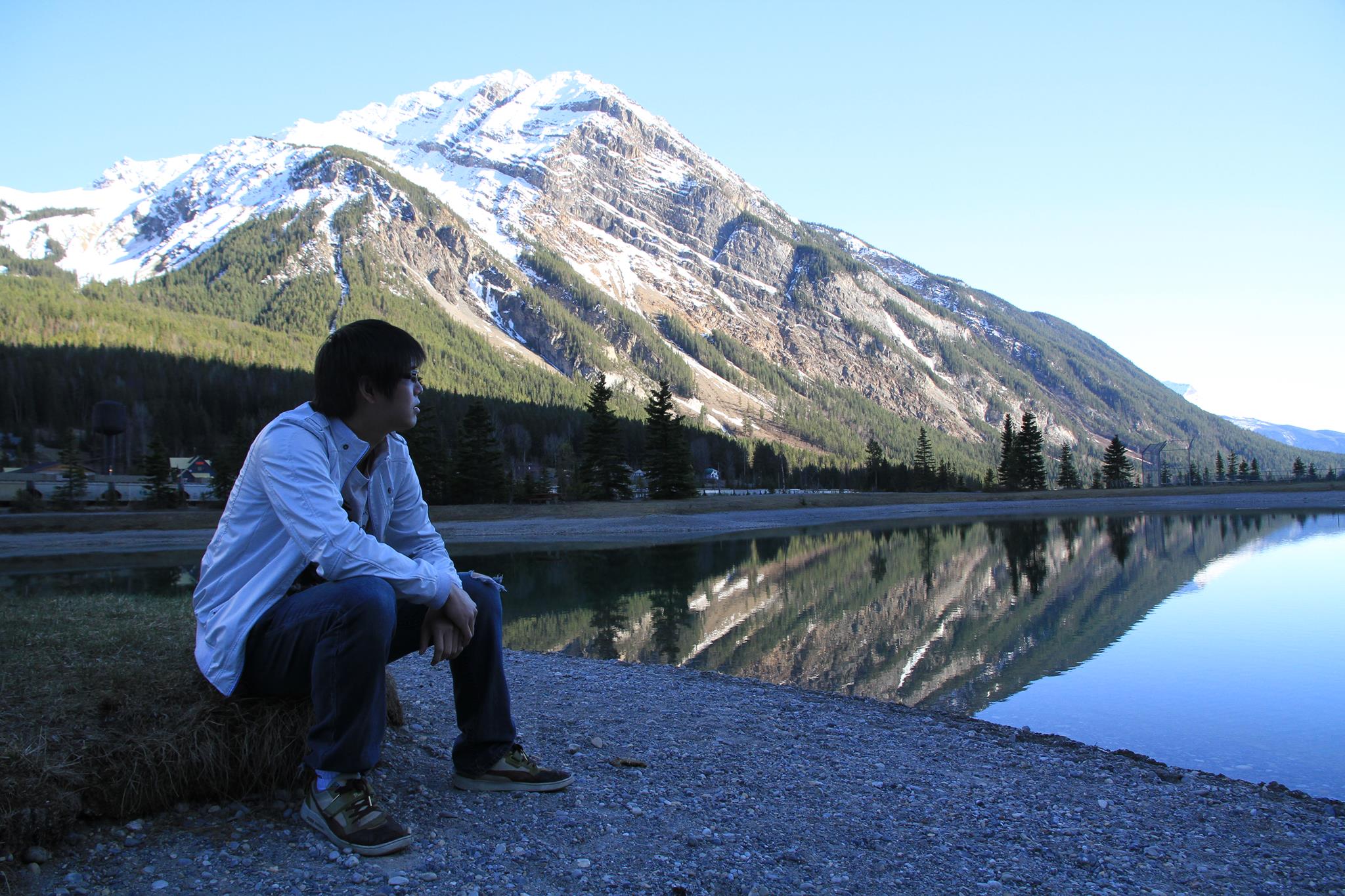 Chris sitting beside a mountain lake with a snowy peak reflected in the water